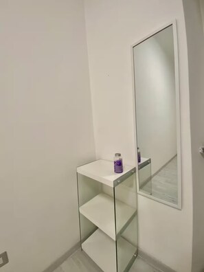 A bathroom with a white vanity, a mirror, and a glass shelf.