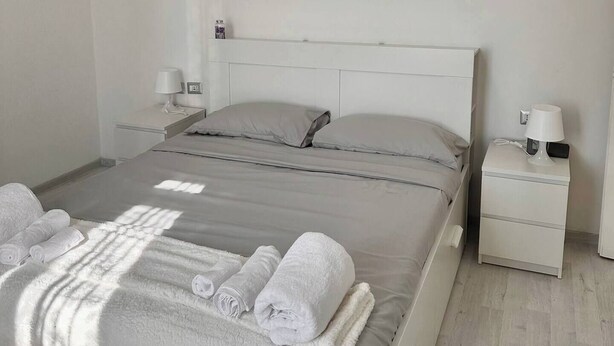 A hotel room with a bed, bedside tables, a lamp, and an air conditioning unit.