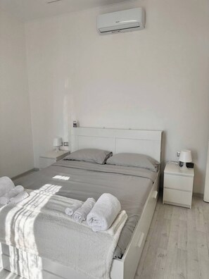 Una camera d'albergo con un letto, comodini, una lampada e un condizionatore d'aria.