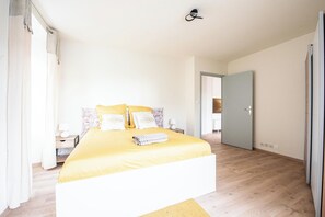 A bedroom with a bed, a nightstand, a lamp, and a door. - Mulhouse by Hardt (Mulhouse)
