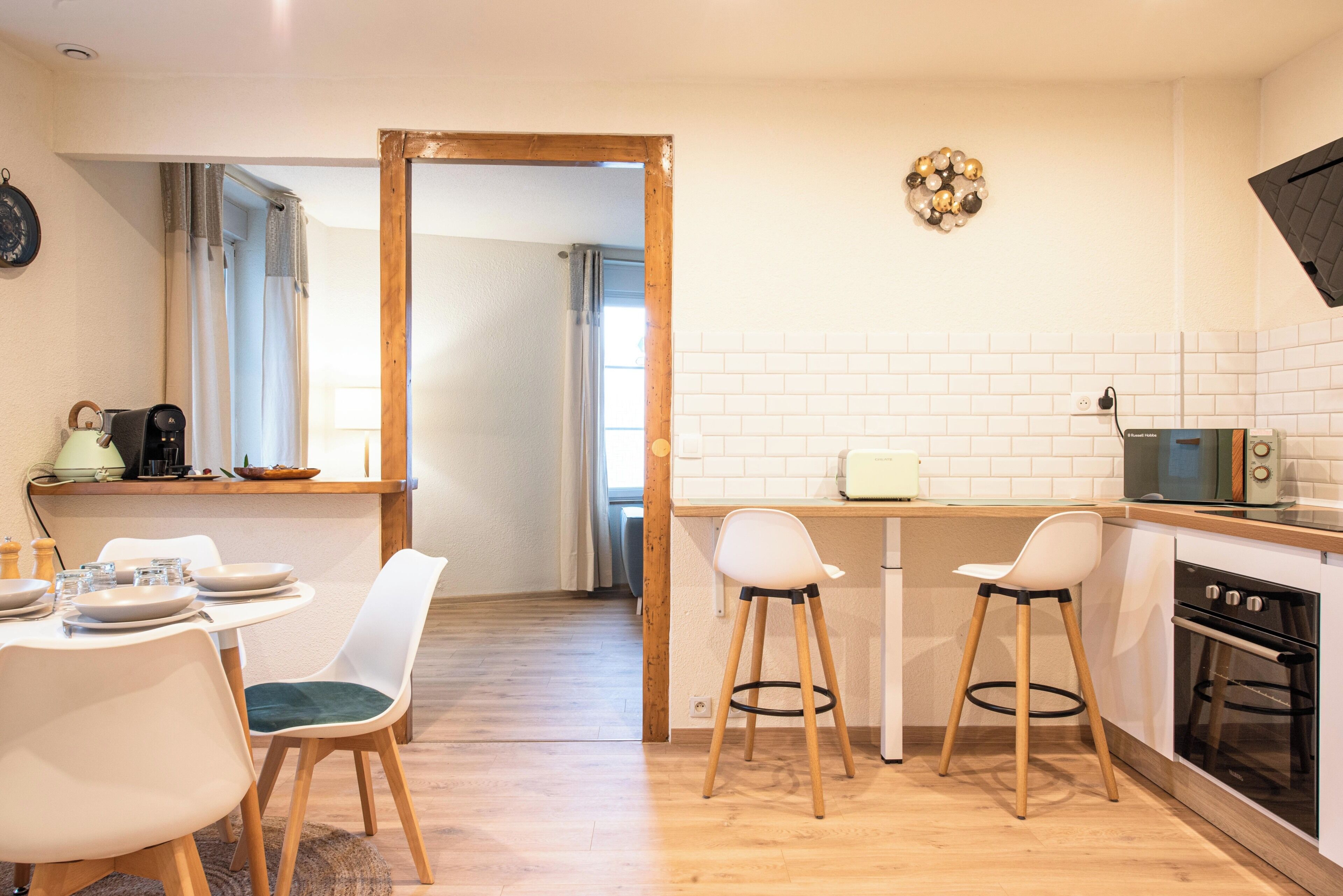 Eine moderne Küche mit weißen Ziegelsteinplatten, einem Holzespeisebereich mit Stühlen, einer Mikrowelle und einem Backofen.