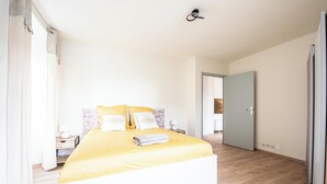 Un dormitorio con cama, mesitas de noche, una lámpara de pared y una puerta.