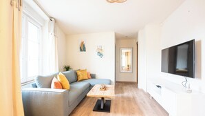 Una sala de estar moderna con un sofá gris, una mesa de centro de madera y un televisor de pantalla plana montado en la pared.