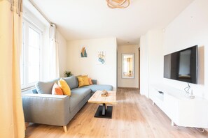 A modern living room with a grey sofa, wooden coffee table, and a flat-screen TV mounted on the wall.