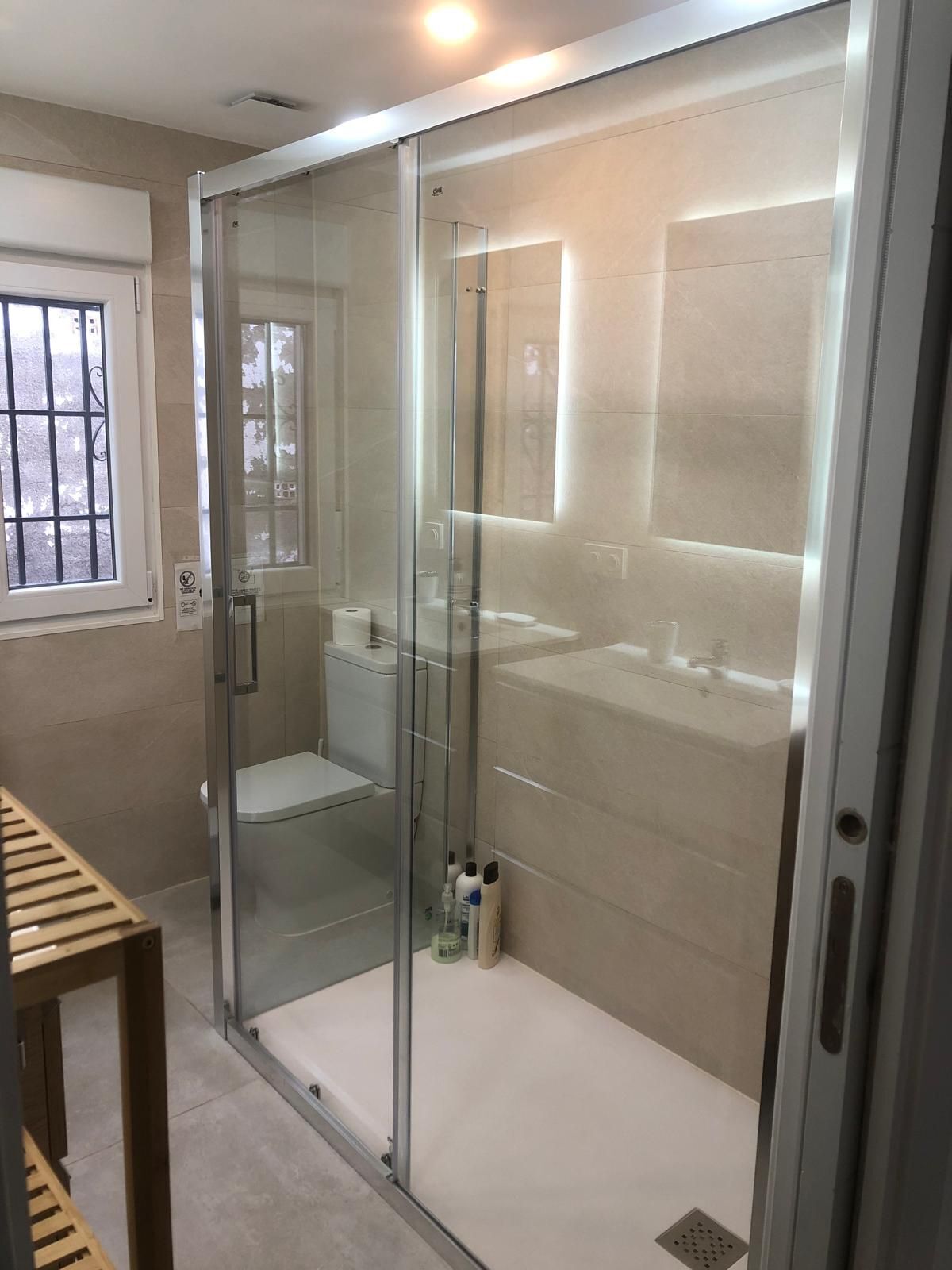 A modern bathroom with a glass-enclosed shower, a toilet, and a sink.