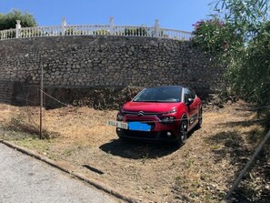 A red car parked on a dirt path with a stone wall and a white fence in the background.