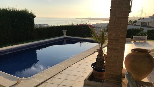 Ein Pool mit Meerblick, umgeben von einer gefliesten Terrasse und Blumentöpfen.
