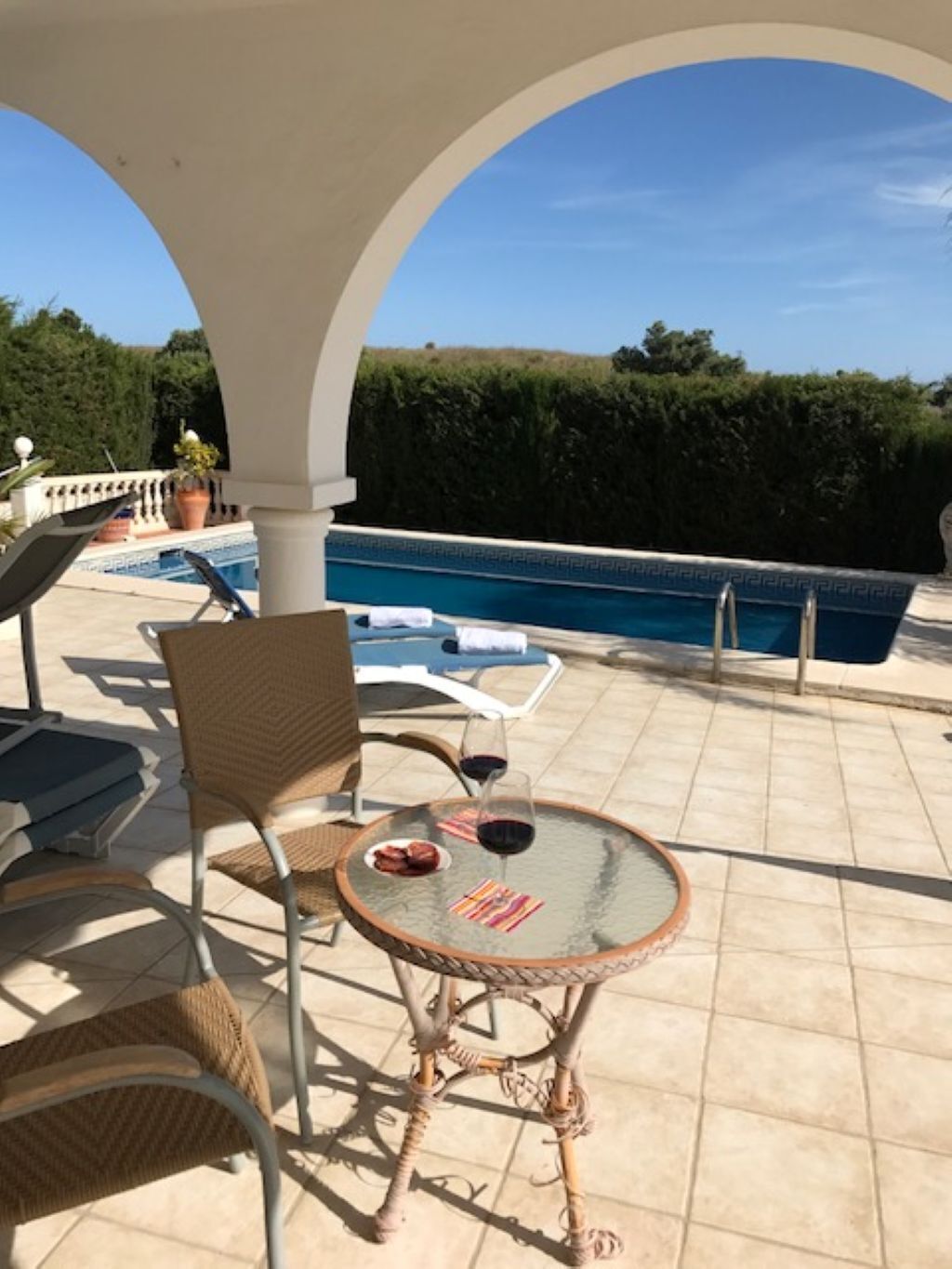 Un espace extérieur abrité comprenant une piscine, des chaises longues et une table avec une bouteille de vin rouge.
