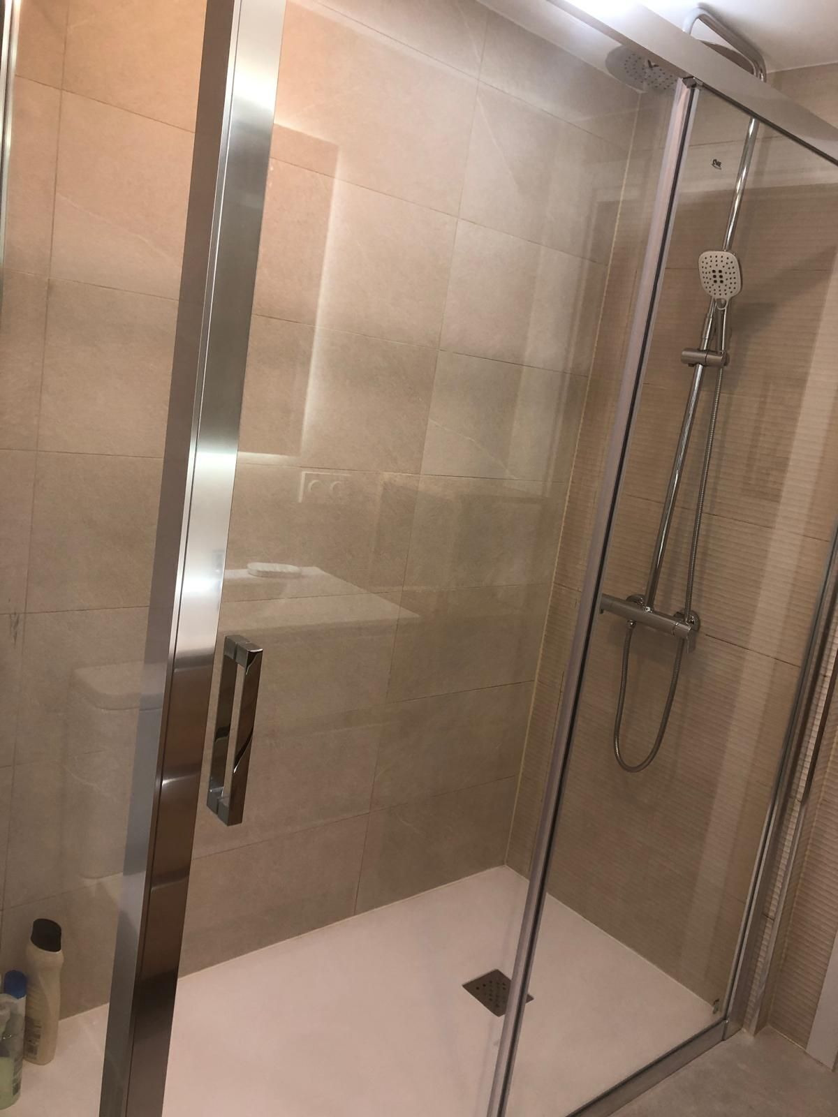 Una ducha moderna con puerta de vidrio, cabezal de ducha manual y un rociador de mano.