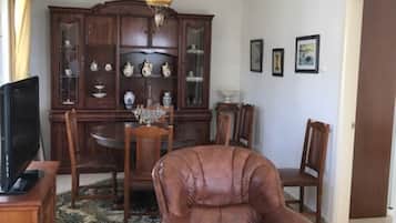 A living room with a brown leather armchair, a wooden cabinet with glass doors, a television, and a dining table with chairs.