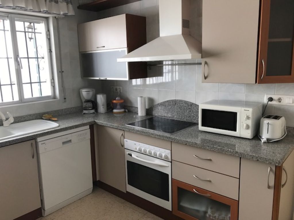 A kitchen with a dishwasher, oven, microwave, toaster, and a window with curtains.