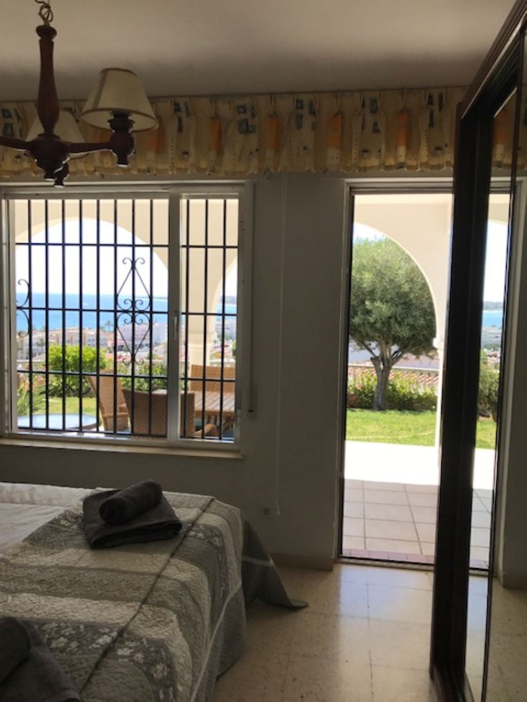 Habitación de hotel con cama, ventana con rejas, vista al mar y puerta que da al exterior.