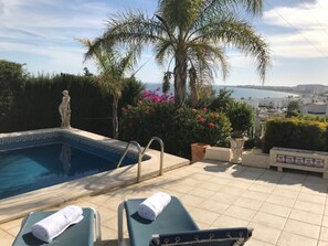A pool area with lounge chairs and a statue, surrounded by palm trees and flowers.