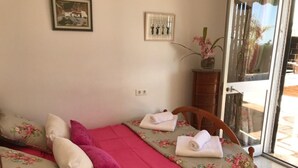 Ein Schlafzimmer mit einem Bett, Kissen, einer Vase mit Blumen und einer Tür zu einem Außenbereich.