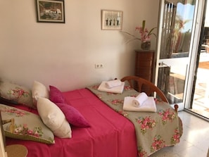 A bedroom with a bed, pillows, a vase with flowers, and a door leading to an outdoor area.
