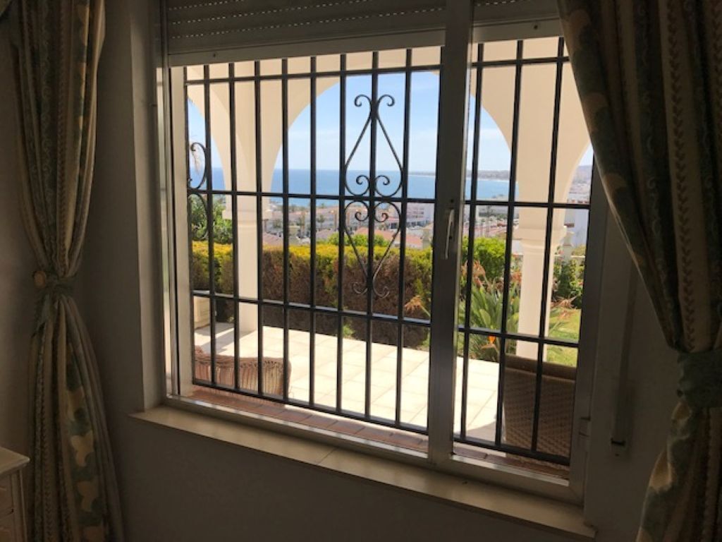 Ventana con barrotes de metal, cortinas y vista a un área exterior ajardinada.