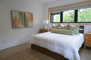 A bedroom with a bed, a nightstand, a window, and two wall-mounted artworks.