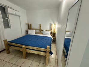 A bedroom with a wooden bed frame, a blue mattress, and a white wall. - Enjoyable 2-bedroom apartment w/full AC in Combate. Pool, generator & water tank (Combate)