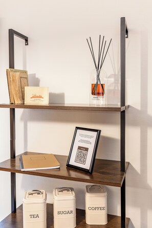 A shelf with a book, a perfume bottle, a framed QR code, and labeled containers for tea, sugar, and coffee. - La Mansarda in Oltretorrente, a cozy retreat among the rooftops of Parma (Parma)