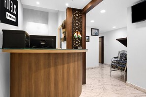 A reception desk with a wooden finish, a black computer, and a decorative panel with flags. - Hotel O Ripon Street SR Royale (Kolkata)
