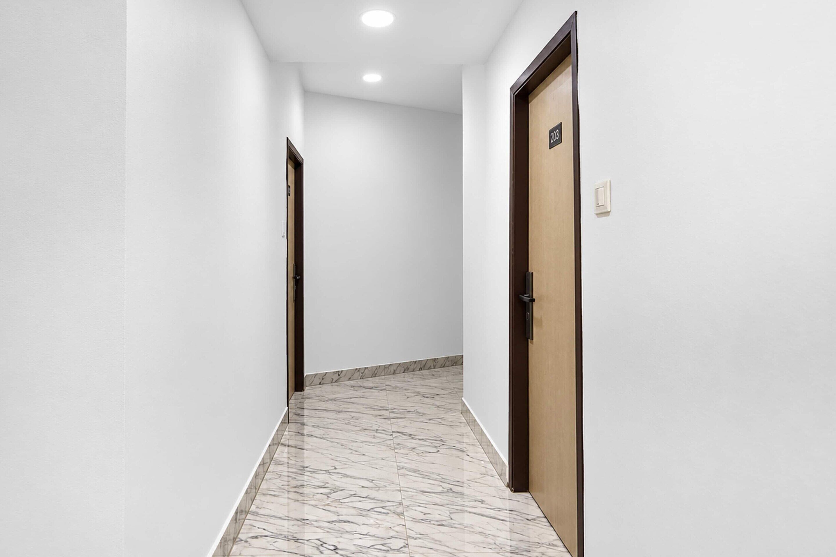 A hallway with white walls, a marble floor, and two doors, one with a number sign.
