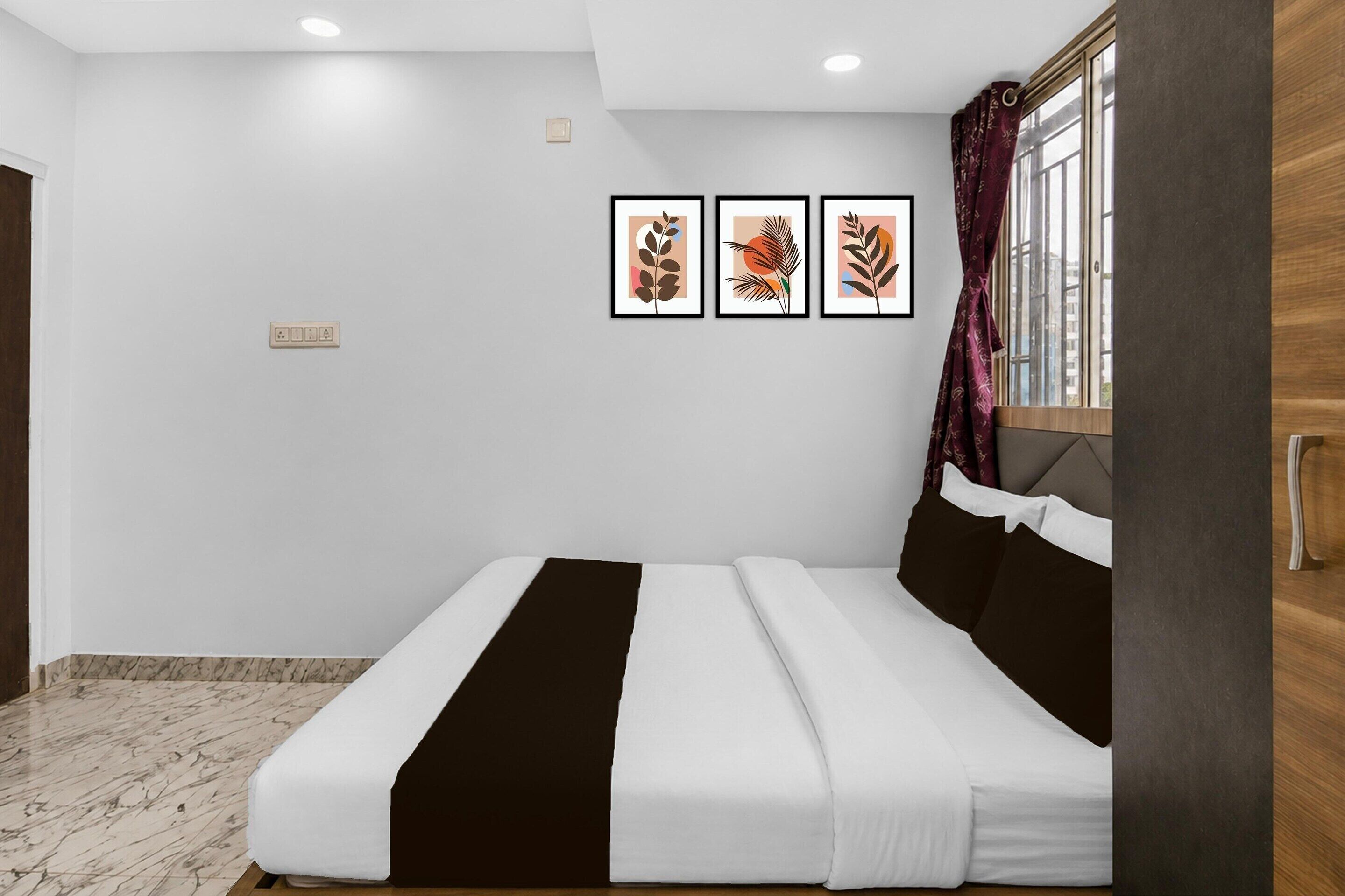 A bedroom with a bed, a window with curtains, and three framed pictures on the wall.
