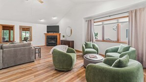 Una sala de estar moderna con chimenea, sillones verdes, un sofá y una televisión.