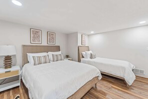 Een hotelkamer met twee bedden, een nachtkastje met een lamp en kunstwerken in een lijst aan de muur.