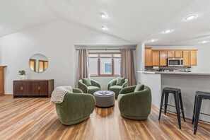 A modern living room with green armchairs, a round ottoman, and a wooden cabinet.