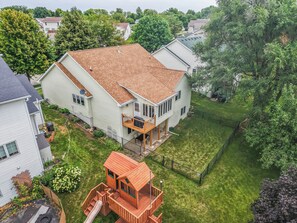 A residential property with a two-story house, a fenced backyard, and a wooden playhouse.