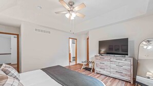 Un dormitorio con una cama, televisión, cómoda y ventilador de techo.