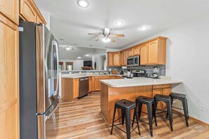 A kitchen with wooden cabinets, a stainless steel refrigerator, a microwave, a dishwasher, and a bar stool area.