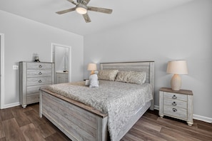 A bedroom with a wooden bed, two bedside tables, a ceiling fan, and a dresser. - Sea La Vie at OIB | Townhome Near Golf & Beaches (Ocean Isle Beach)