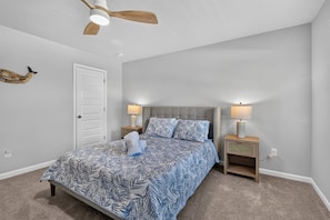 A bedroom with a bed, two bedside tables, a ceiling fan, and a door.
