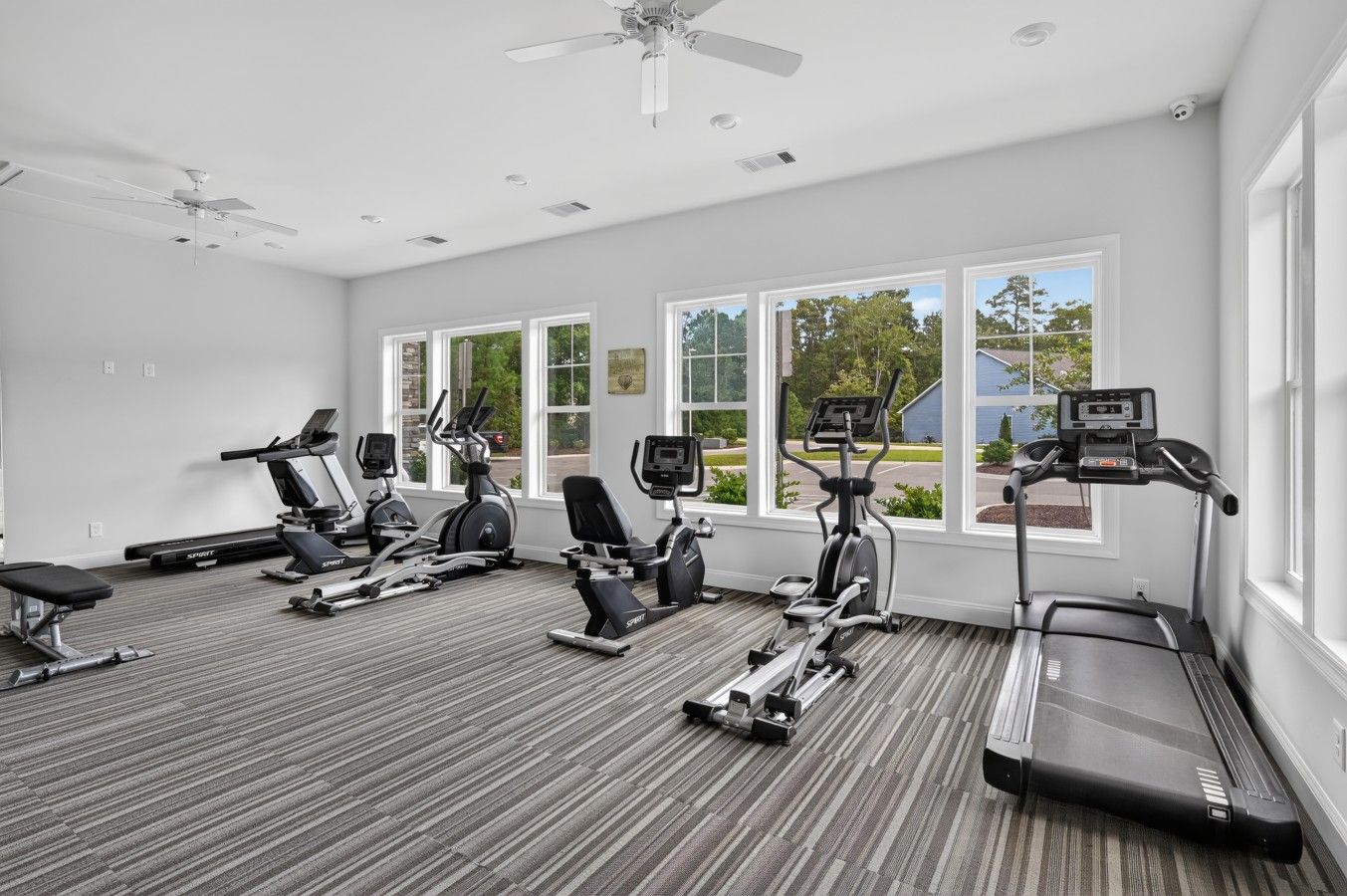 A gym with various exercise equipment, large windows, and a ceiling fan.