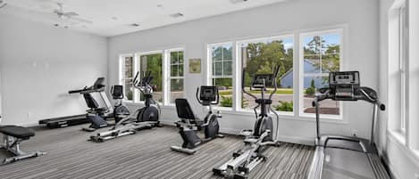 Un gimnasio con diverso equipo de ejercicio, amplias ventanas y un ventilador de techo.