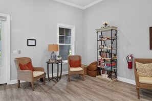 A living room with two wicker chairs, a small table with a lamp, a bookshelf, and a fire extinguisher on the wall.