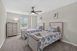 Ein Schlafzimmer mit zwei Betten, einem Schminktisch, einem Deckenventilator und einem Fenster mit Jalousien.