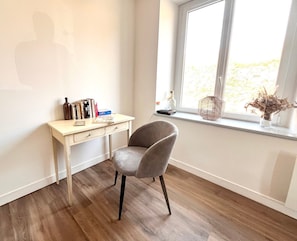 Ein Zimmer mit Schreibtisch, Stuhl und einem Fenster mit Blick.