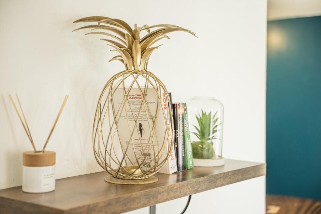 Uma lâmpada decorativa em formato de abacaxi sobre uma estante com livros e uma pequena planta ao lado.