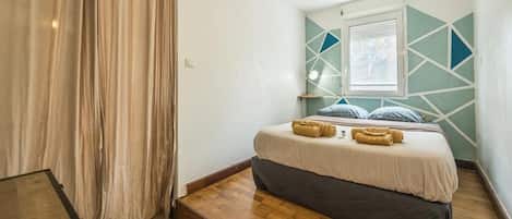 A bedroom with a bed, a window, and a geometric wall design.