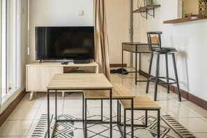 Un espacio habitable moderno con una televisión de pantalla plana sobre un soporte de madera, una mesa de comedor con sillas y una zona de bar con taburetes.