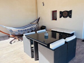 A patio area with a glass-top table, wicker chairs, a hammock, and a dartboard. - A Cottage Amid the Birdsong. Beautiful views and tranquility, 300 meters from Flow Vélo (Chazelles)