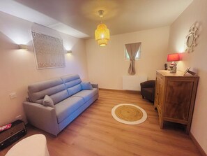 A living room with a sofa, a wooden cabinet, a rug, a hanging light fixture, and a wall-mounted artwork. - A Cottage Amid the Birdsong. Beautiful views and tranquility, 300 meters from Flow Vélo (Chazelles)