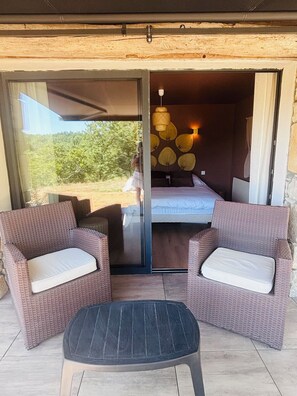 A room with a bed, two wicker chairs with cushions, a small table, and a view of the outdoors. - A Cottage Amid the Birdsong. Beautiful views and tranquility, 300 meters from Flow Vélo (Chazelles)