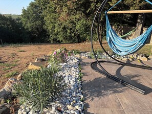 A hammock suspended between two metal poles, a garden bed with pebbles and plants, and a paved walkway. - A Cottage Amid the Birdsong. Beautiful views and tranquility, 300 meters from Flow Vélo (Chazelles)
