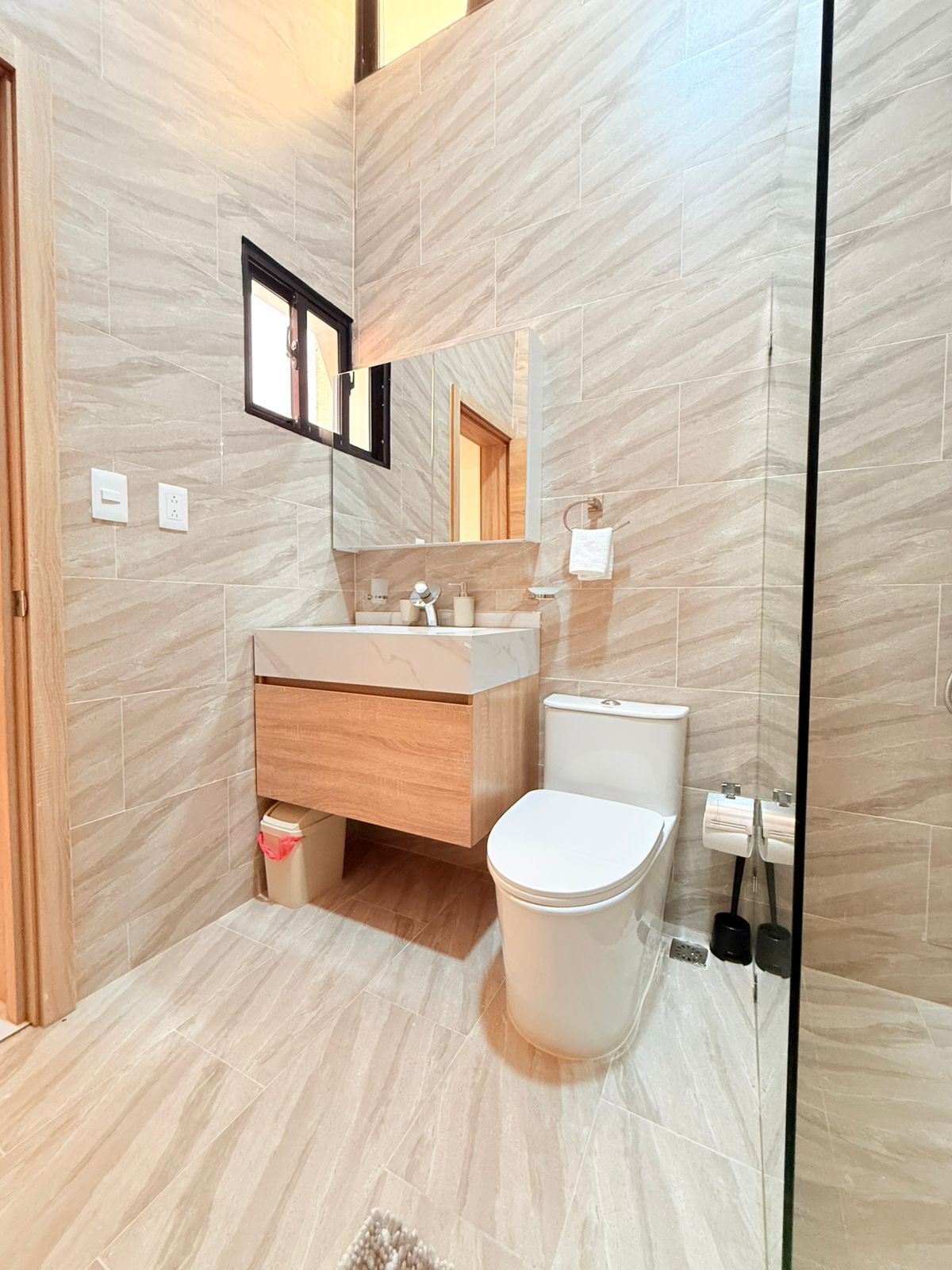 A modern bathroom with a marble floor, a wooden vanity, a white toilet, and a large mirror.