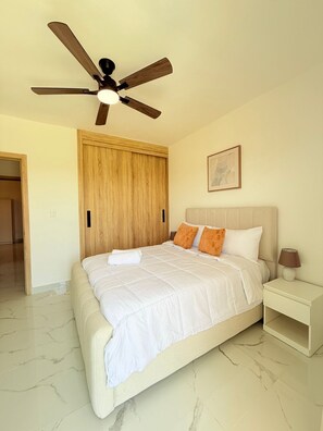 Une chambre à coucher comprenant un lit, une table de chevet, un ventilateur de plafond, une armoire en bois et un tableau encadré accroché au mur.