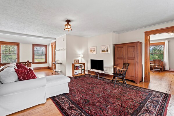 A spacious living room with a white sofa, a red patterned rug, a television, and a wooden cabinet. - Belclare - Vineyard Estate (Northport)