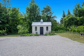 A small, single-story building with a metal roof, surrounded by a gravel driveway and a variety of trees. - Belclare - Vineyard Estate (Northport)